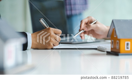 Real estate agent with house model hand putting signing contract, hands holding pen to sign a contract close up. Real estate agent with house model hand putting signing contract, hands holding pen to sign a contract close up. 88219785