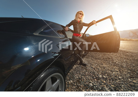 Portrait of a stylish attractive Caucasian young woman getting out of a retro sports car in the mountains at sunset. Travel concept copy space Portrait of a stylish attractive Caucasian young woman getting out of a retro sports car in the mountains at sunset. Travel concept copy space 88222209