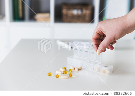 Closeup of female elderly hands sorting pills. Medical pill box with doses of tablets for daily take with white, yellow, beige drugs and capsules. Young woman getting her daily vitamins at home Closeup of female elderly hands sorting pills. Medical pill box with doses of tablets for daily take with white, yellow, beige drugs and capsules. Young woman getting her daily vitamins at home 88222666