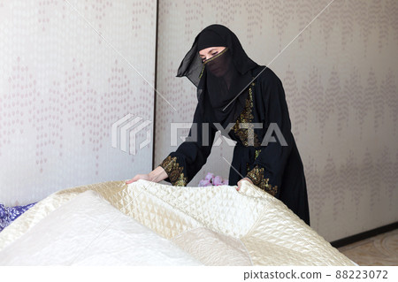 Muslim woman housewife lays a bedspread on the bed Muslim woman housewife lays a bedspread on the bed 88223072