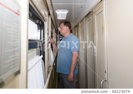 A male train passenger stands in the carriage corridor and reads the route and timetable A male train passenger stands in the carriage corridor and reads the route and timetable 88223074