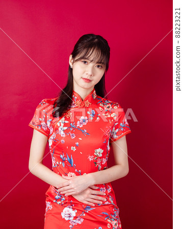 Portrait of a young asian woman in traditional cheongsam qipao dress having a stomach ache isolated over red background. Portrait of a young asian woman in traditional cheongsam qipao dress having a stomach ache isolated over red background. 88223221