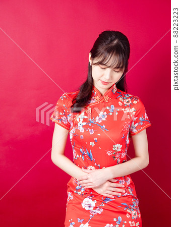 Portrait of a young asian woman in traditional cheongsam qipao dress having a stomach ache isolated over red background. Portrait of a young asian woman in traditional cheongsam qipao dress having a stomach ache isolated over red background. 88223223
