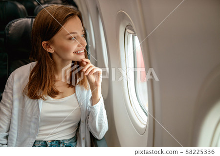 Joyful woman looking out the window in airplane Joyful woman looking out the window in airplane 88225336