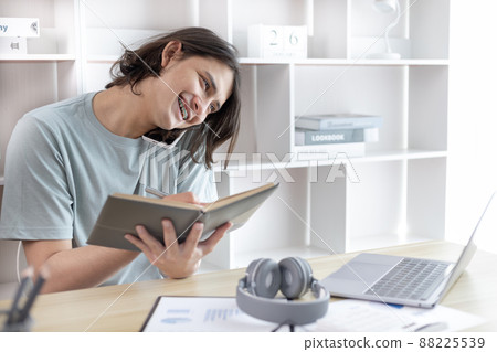Asian male worker talking on phone and working on laptop with smiling face, Office staff work and telephone conversations, Take notes for reminders, Business conversation over the phone. Asian male worker talking on phone and working on laptop with smiling face, Office staff work and telephone conversations, Take notes for reminders, Business conversation over the phone. 88225539