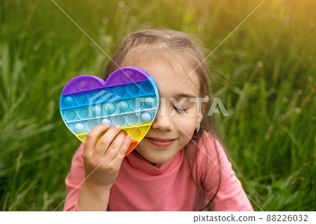A little cute girl is playing with a modern popit toy. A fascinating sensory toy for the development . Colorful and bright pop it toy in the form of a heart. Simple dimple A little cute girl is playing with a modern popit toy. A fascinating sensory toy for the development . Colorful and bright pop it toy in the form of a heart. Simple dimple 88226032