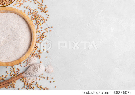 Buckwheat flour in a wooden bowl with wooden spoon and raw green buckwheat grain in a bowl on grey stone background Buckwheat flour in a wooden bowl with wooden spoon and raw green buckwheat grain in a bowl on grey stone background 88226073