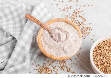 Buckwheat flour in a wooden bowl with wooden spoon and raw green buckwheat grain on grey stone background, top view Buckwheat flour in a wooden bowl with wooden spoon and raw green buckwheat grain on grey stone background, top view 88226080