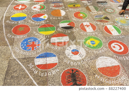 Hand of teenager drawing multi-colored flags of different countries in circles on pavement with multi-colored crayons 88227400