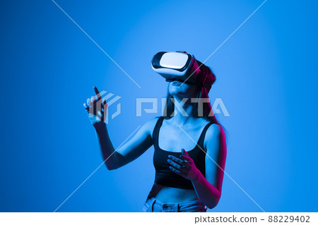 Close up of young woman stands in studio wearing VR glasses and swiping scrolling zooming with hands in a virtual space while interacting with a objects in a metaverse. Virtual reality technology. Close up of young woman stands in studio wearing VR glasses and swiping scrolling zooming with hands in a virtual space while interacting with a objects in a metaverse. Virtual reality technology. 88229402