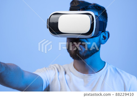 Young man using VR headset helmet to play simulation game. Watching virtual reality 3d video. Bearded man in VR goggles looking around. 88229410