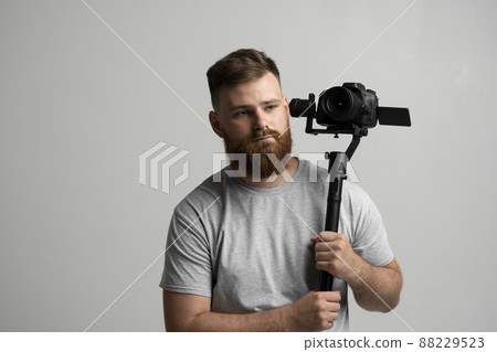 Professional bearded videographer holding camera which set on 3-axis gimbal. Videographer using steadicam. Pro equipment helps to make high quality video without shaking. 88229523