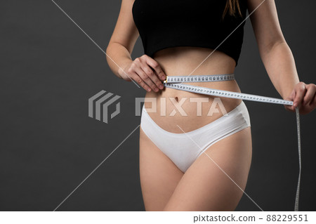 Healthy sporty slim female measures her waist with a measuring tape. Healthy fitness and eating lifestyle concept. 88229551