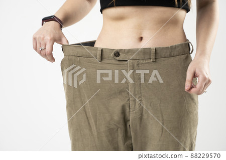 Diet concept and weight loss. Beautiful sporty woman showing how much weight she loss wearing old big jeans. Healthy lifestyles. 88229570