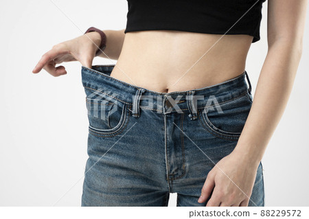 Woman in blue oversize jeans showing a result of weight loss on white background. Diet concept and weight loss. 88229572