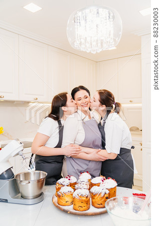 mother and daughters with Kraffins, easter cakes and Panettones in the kitchen. mother and daughters with Kraffins, easter cakes and Panettones in the kitchen. 88230003
