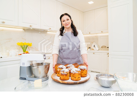 female cook with Kraffins, easter cakes and Panettones in the kitchen. female cook with Kraffins, easter cakes and Panettones in the kitchen. 88230008