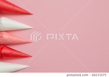 Multicolored glazing in icing bags on the pink table. Set for decorating desserts. Icing for gingerbread, brownies and cakes in pastry bags. Cake decorating tools. 88231075