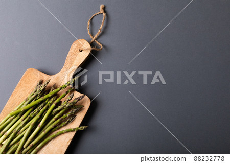 Overhead view of fresh asparagus on wooden cutting board by copy space against gray background Overhead view of fresh asparagus on wooden cutting board by copy space against gray background 88232778