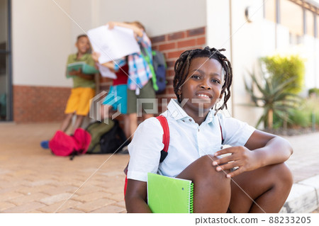 Portrait of african american elementary schoolboy with books while sitting on floor in school Portrait of african american elementary schoolboy with books while sitting on floor in school 88233205
