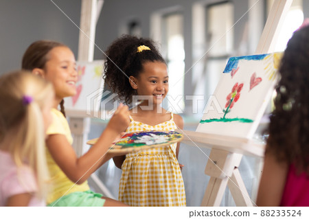 Cheerful multiracial elementary schoolgirls standing by caucasian girl painting on easel in class Cheerful multiracial elementary schoolgirls standing by caucasian girl painting on easel in class 88233524
