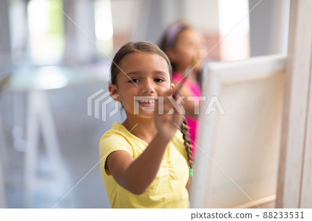 Portrait of smiling caucasian girl painting on easel during drawing class in school 88233531