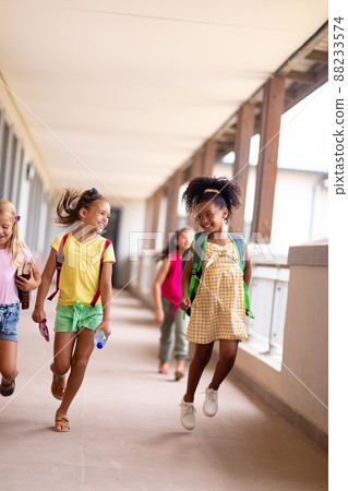 Full length of cheerful multiracial elementary schoolgirls walking in corridor Full length of cheerful multiracial elementary schoolgirls walking in corridor 88233574