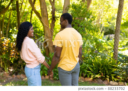 Smiling african american mid adult couple looking at each other while holding hands in backyard Smiling african american mid adult couple looking at each other while holding hands in backyard 88233702