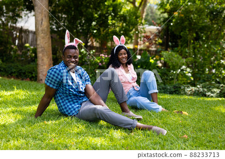Portrait of happy african american mid adult couple wearing bunny ears while sitting in backyard Portrait of happy african american mid adult couple wearing bunny ears while sitting in backyard 88233713