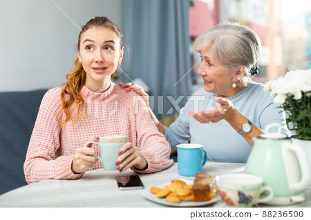 Young woman enjoying conversation with elderly mother over cup of coffee 88236500
