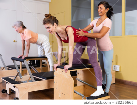 Hispanic woman pilates instructor helping girl exercising on combo chair 88236665