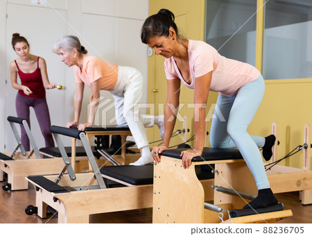 Female instructor helps women perform an exercise on a combined chair Female instructor helps women perform an exercise on a combined chair 88236705