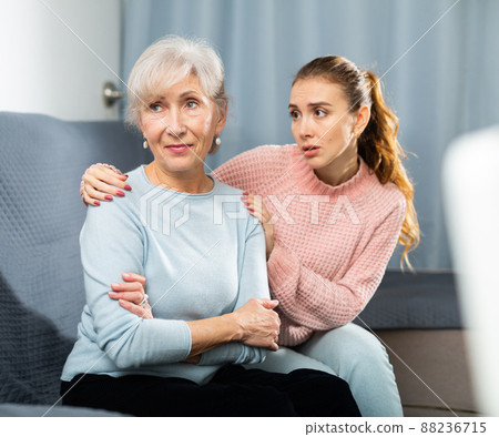 Adult daughter asking for forgiveness from upset elderly mother on sofa 88236715