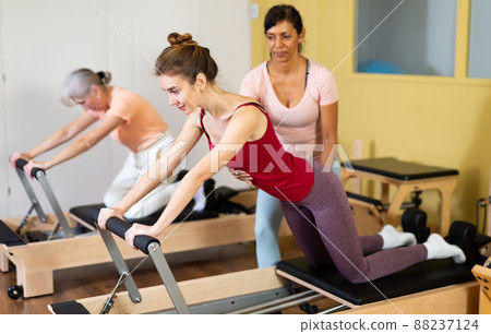 Female trainer controlling young woman doing pilates on reformer Female trainer controlling young woman doing pilates on reformer 88237124