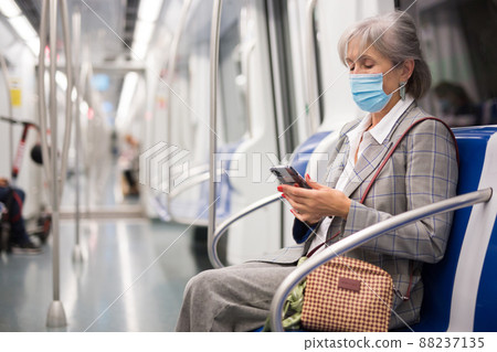 Mature woman in mask with smartphone in subway car 88237135