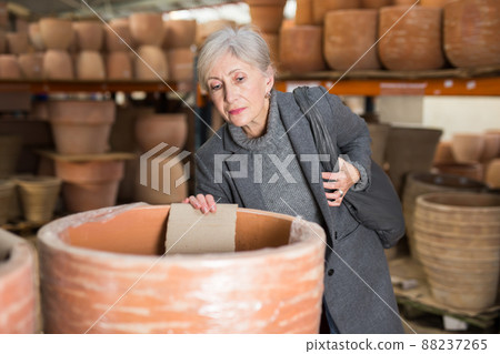 Aged woman selecting decorative earthenware pot in shop 88237265