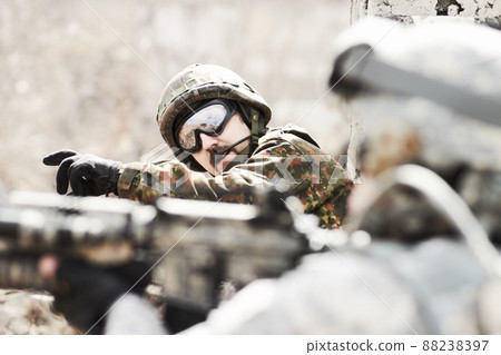 Leading his platoon. Profile of a commandant giving orders to his soldiers while lying flat on the ground with guns in hand. Leading his platoon. Profile of a commandant giving orders to his soldiers while lying flat on the ground with guns in hand. 88238397