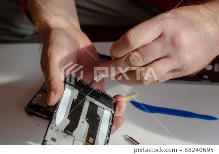 Repair of smartphones concept. A man unscrews the screws fixing the display from the board. Part of a series. Repair of smartphones concept. A man unscrews the screws fixing the display from the board. Part of a series. 88240695