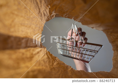 A hand places a shopping cart in a paper bag. A mature man's hand holds an empty shopping cart over an open brown bag. Shot from the bottom up. Close up. Selective focus A hand places a shopping cart in a paper bag. A mature man's hand holds an empty shopping cart over an open brown bag. Shot from the bottom up. Close up. Selective focus 88240713