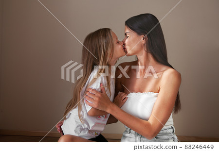 Beautiful mother brunette model kiss on lips daughter with long hair isolate beige background. Natural light, neutral color, Mothers Day Beautiful mother brunette model kiss on lips daughter with long hair isolate beige background. Natural light, neutral color, Mothers Day 88246449