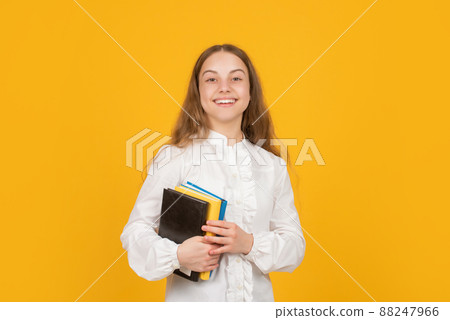 positive teen girl hold school workbook on yellow background, back to school 88247966