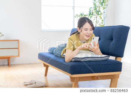 A young woman lying on the sofa in the living room and operating her smartphone 88256463