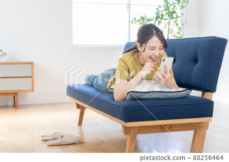 A young woman lying on the sofa in the living room and operating her smartphone A young woman lying on the sofa in the living room and operating her smartphone 88256464