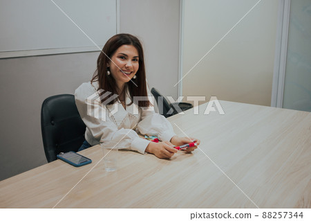Young brunette woman in a white blouse sitting at the table in the office and holding a marker in her hands.. Business Education concept 88257344
