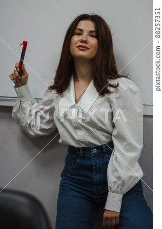Young eductor in a white blouse with a red marker standing in front of a white board. Looks into the camera Young eductor in a white blouse with a red marker standing in front of a white board. Looks into the camera 88257351