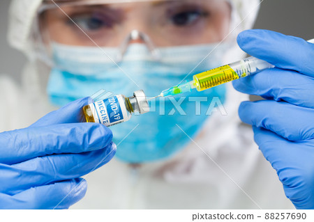 Female medical scientist holding COVID-19 vaccine and syringe jab with yellow liquid 88257690