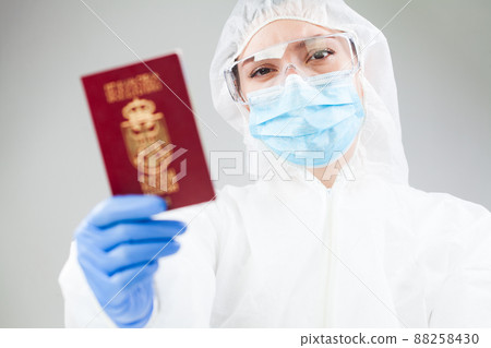 Medical healthcare worker in full personal protective equipment holding red passport Medical healthcare worker in full personal protective equipment holding red passport 88258430