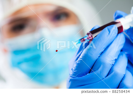 Doctor or lab scientist in personal protective equipment holding syringe full of PRP blood plasma 88258434