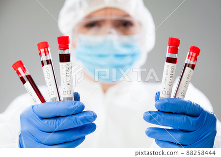 Lab scientist or medical technologist wearing hazmat protective suit and mask holding test tube vacutainers Lab scientist or medical technologist wearing hazmat protective suit and mask holding test tube vacutainers 88258444
