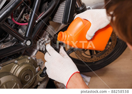 The process of pouring new oil into the motorcycle engine. The process of pouring new oil into the motorcycle engine. 88258538